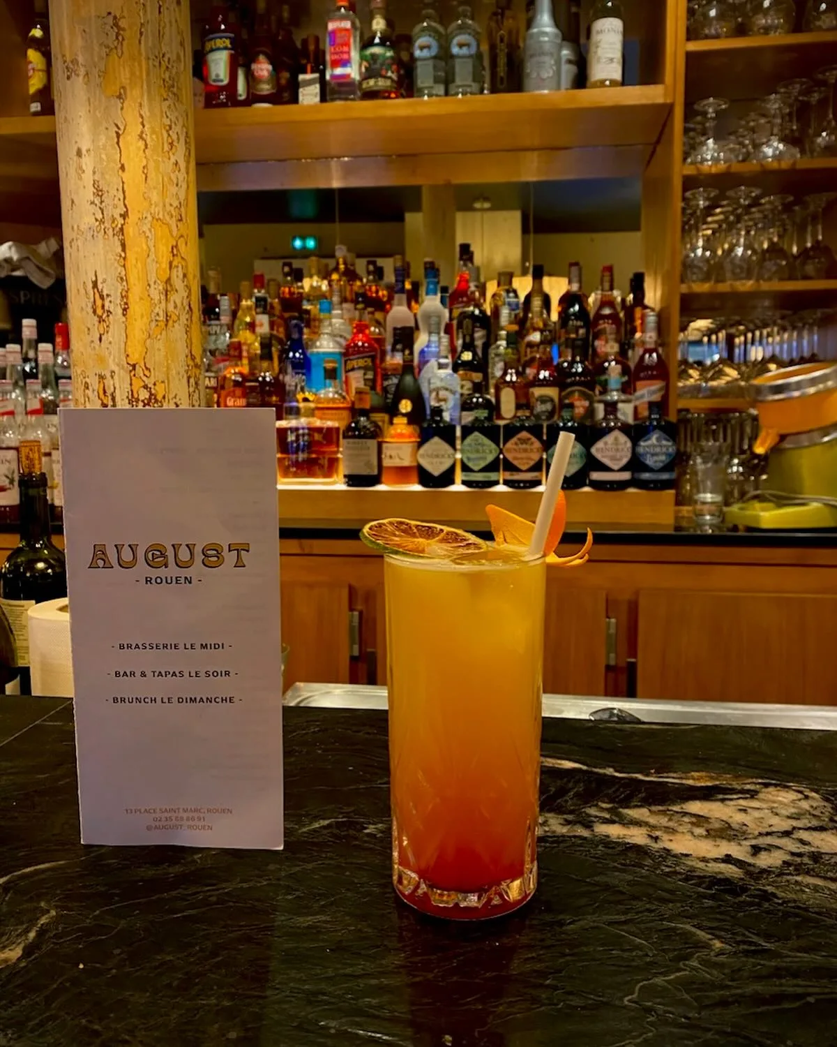 Cocktail signature servi au comptoir d'August, à Rouen, devant l'étagère à spiritueux.