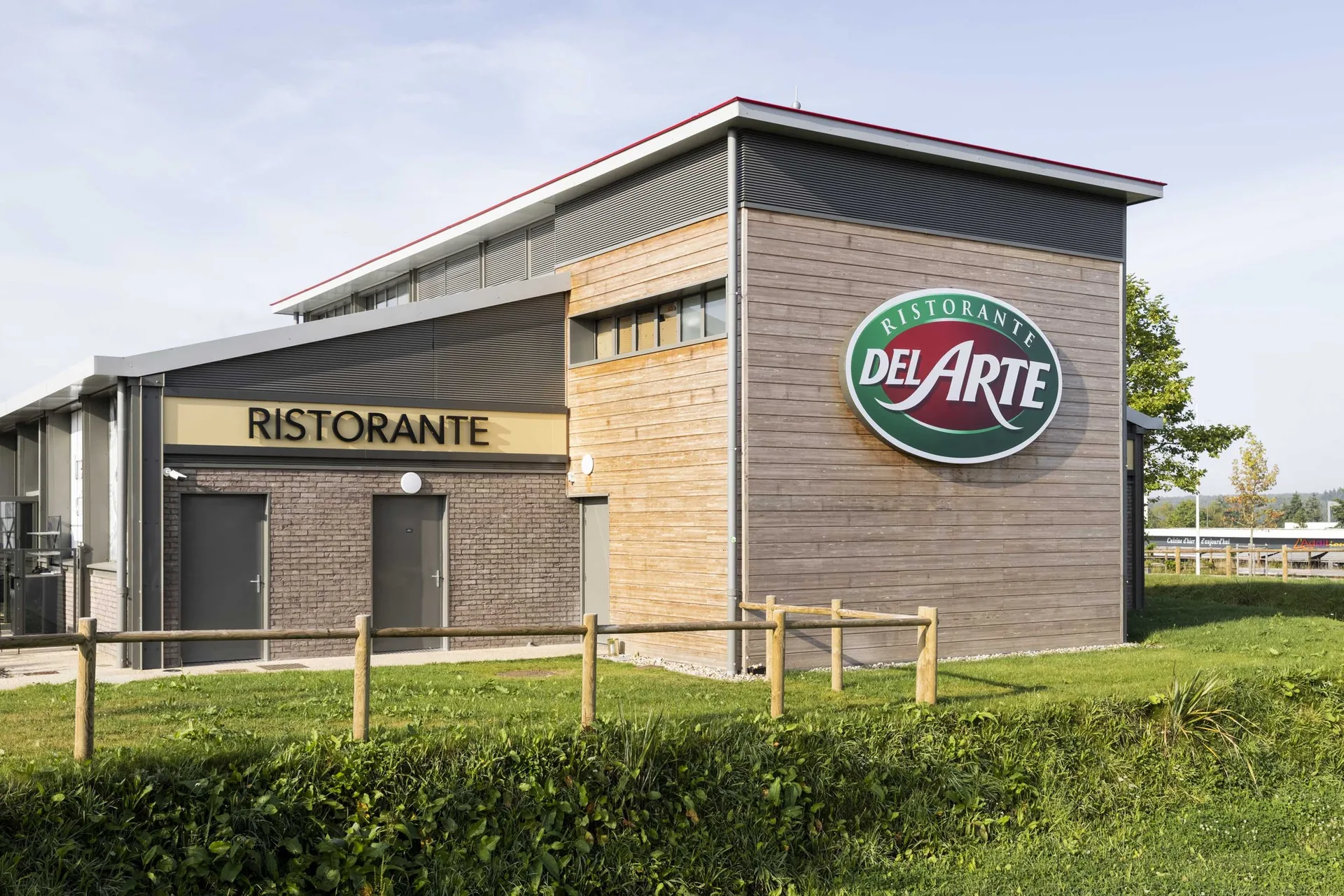 Façade en bois et zinc noir du Del Arte Isneauville avec enseigne ronde rouge Ristorante Del Arte et mention RISTORANTE en lettrage doré sur le bardage en bois