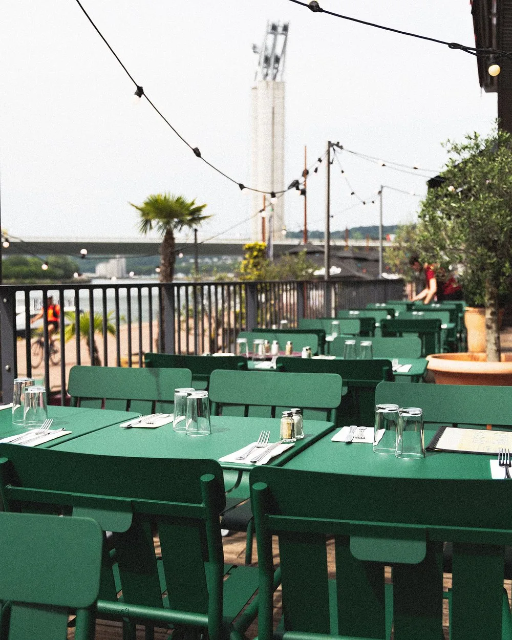 Terrasse de Toto's au bord de la Seine à Rouen, avec tables et chaises vertes sous des guirlandes lumineuses.